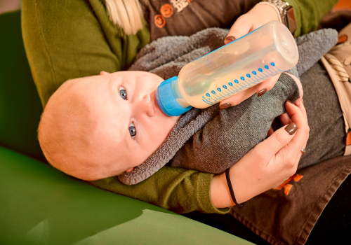 Pedagogisch medewerker geeft baby flesvoeding