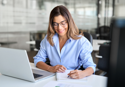 Vrouw volgt een training op haar laptop en maakt aantekeningen
