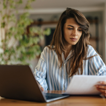 vrouw achter laptop kijkt naar papier