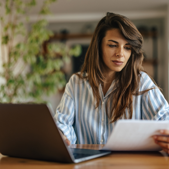 vrouw achter laptop kijkt naar papier