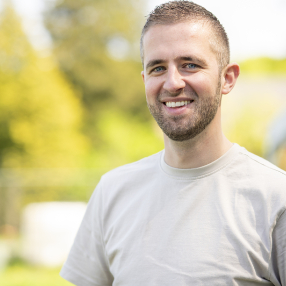 Tom Bisselink staat buiten en kijkt lachend in de camera