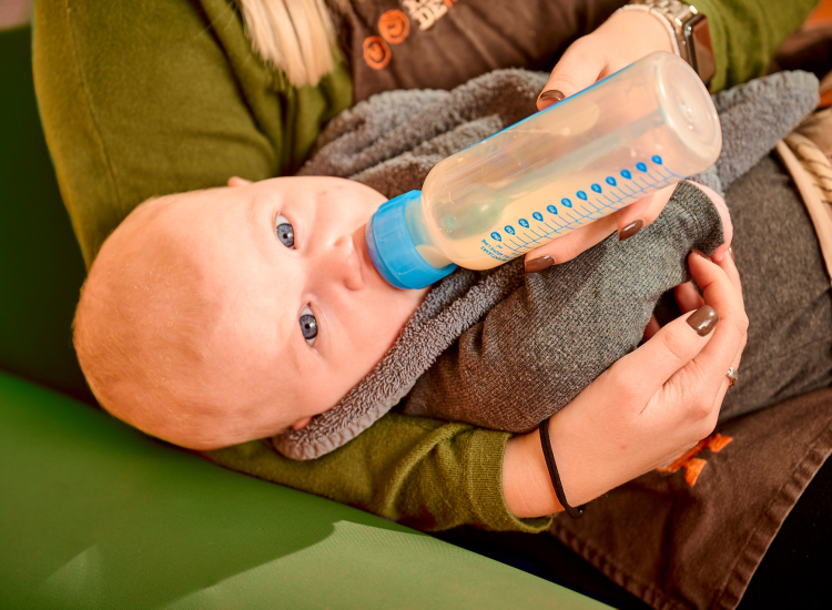 Pedagogisch medewerker geeft baby flesvoeding