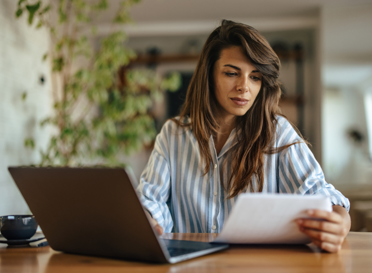 vrouw achter laptop kijkt naar papier